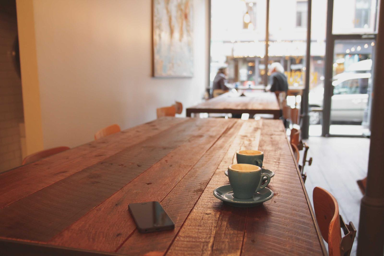 The tasting bar: a long reclaimed-wood table with two small cups, a phone, and a bright window behind