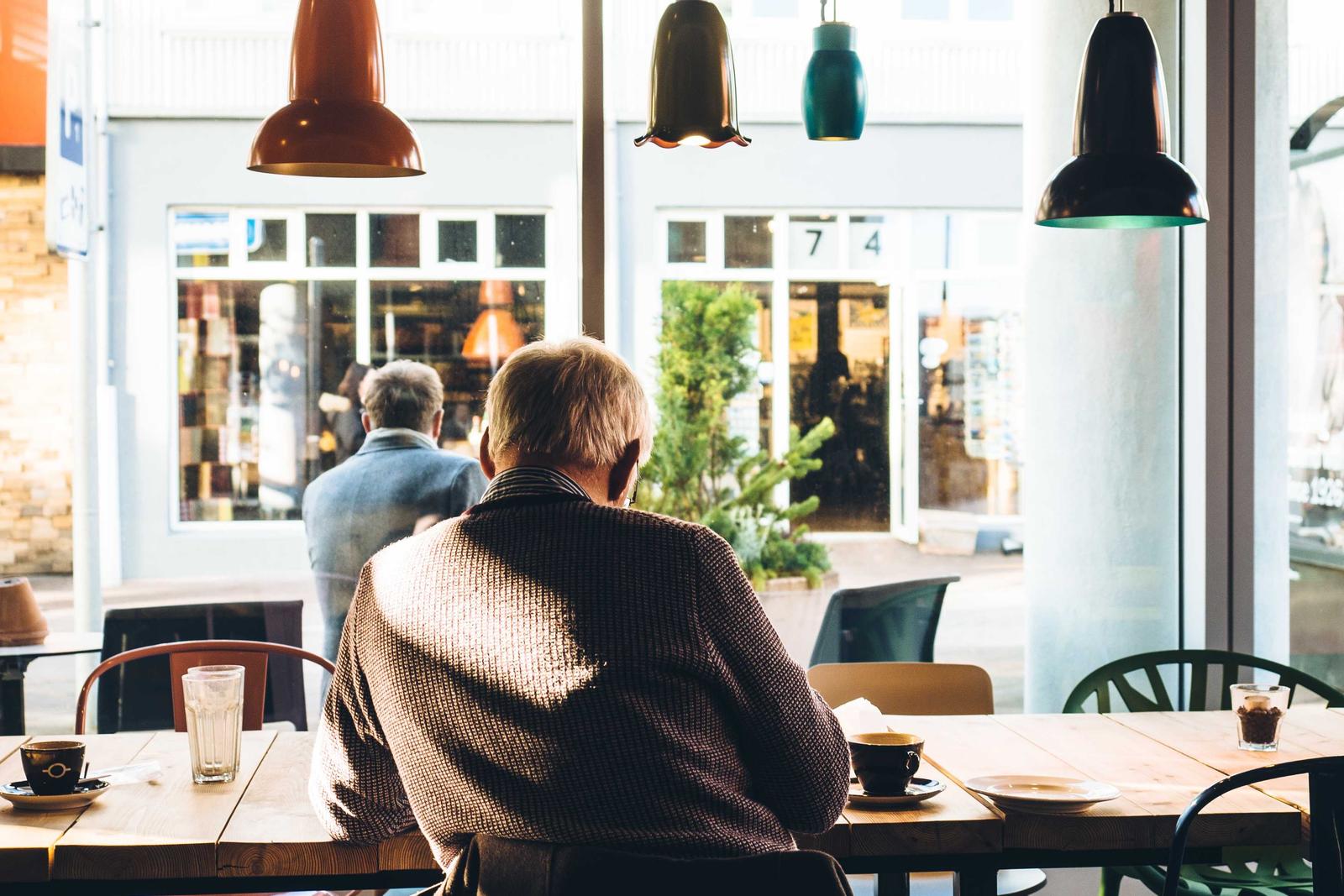 Pendant lamps over a cafe window table, with a customer seated and a street outside