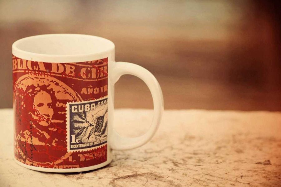 A white mug printed with vintage red postage stamps, resting on a stone ledge