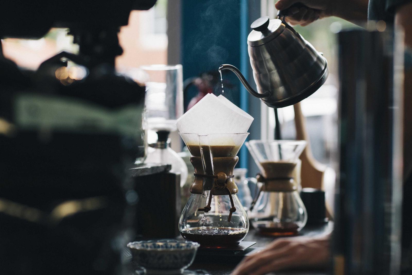 A gooseneck kettle pouring a thin stream into a paper filter set in a Chemex